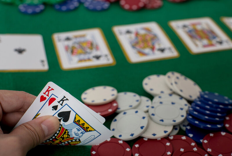 Hand holding two playing cards with poker chips and playing cards on table