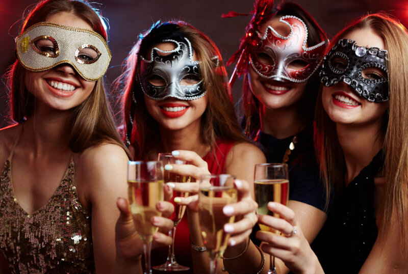 Four women in masquerade masks holding champagne glasses