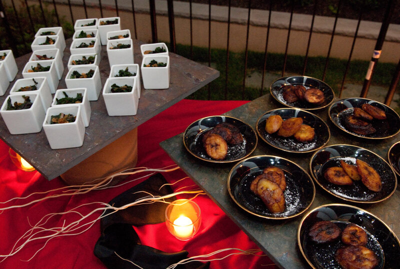 Plates of plantains and cups of vegetables on table with red table cloth and light decorations