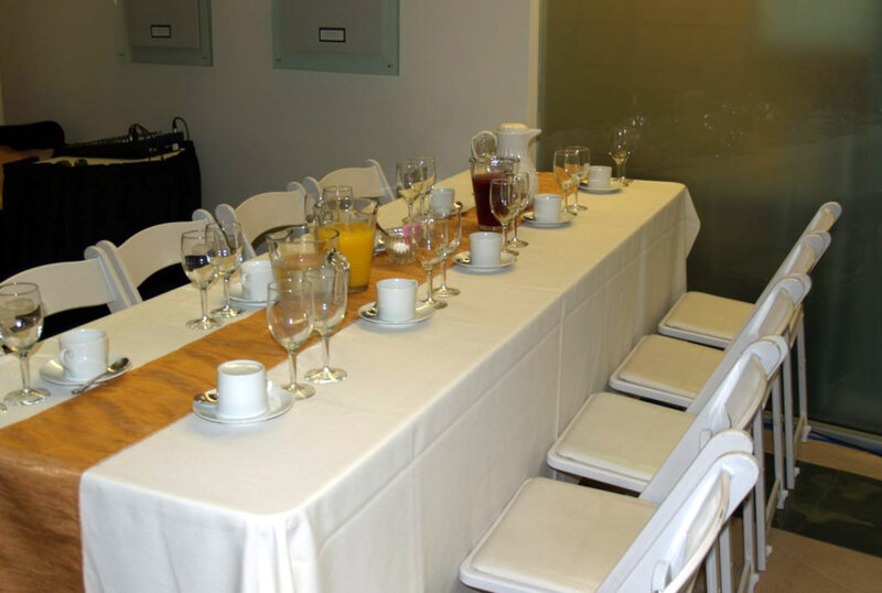 Long table with white table cloth with coffee cups, pitchers of juice and wine glasses